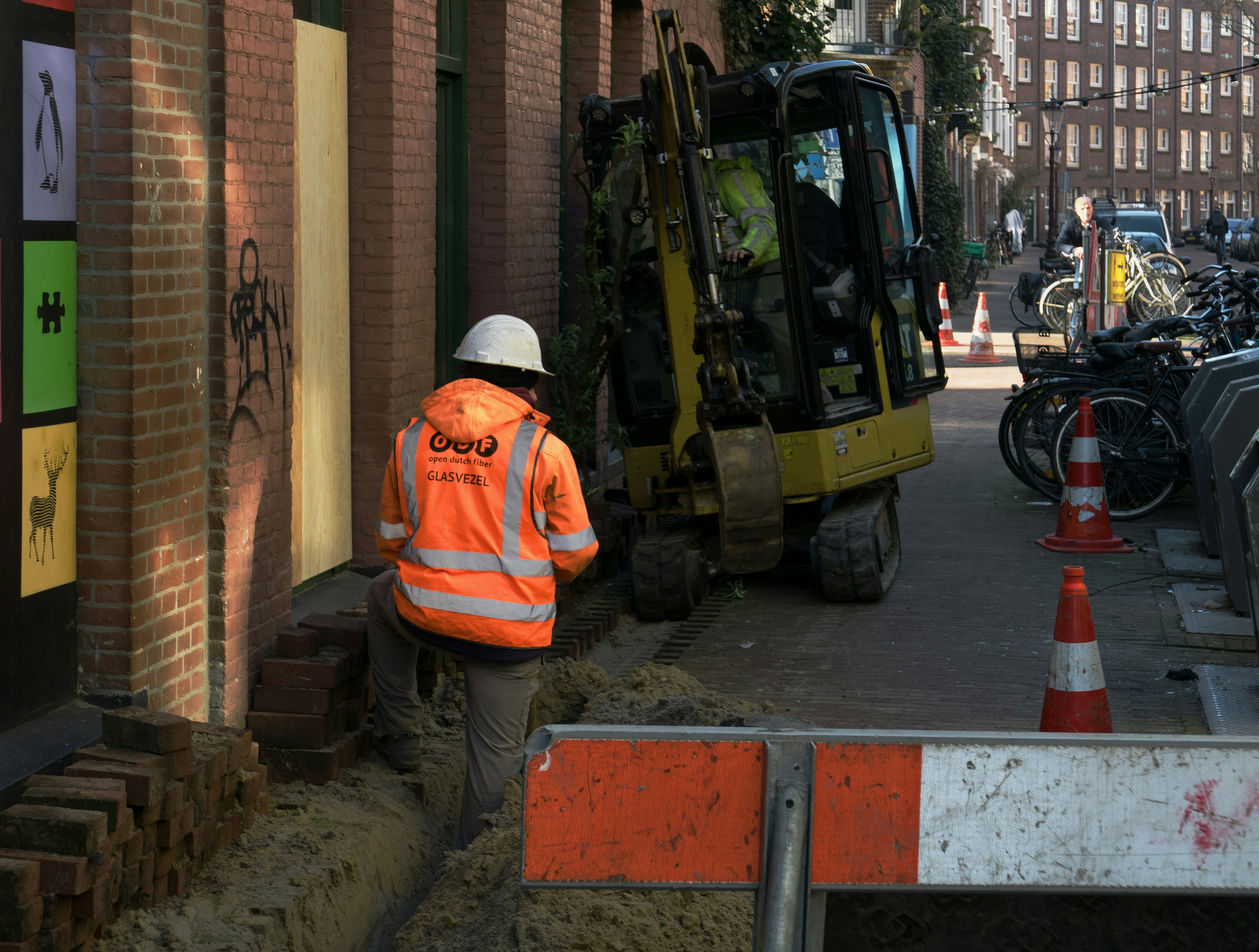 Free photo Amsterdam city - road workers, digging in the sidewalk of the street to create the new fiber optic network in the grounds. It is work in a narrow old street on a sunny day, so navigation is a hard job. Location is in the neighbourhood Kinkerbuurt. Urban street photography in free images – free download images for poster or wallpaper, photos in The Netherlands by Fons Heijnsbroek. . Gratis foto van straat werkers die glasvezel aanleggen in de Hasebroekstraat in de Kinkerbuurt. Zon en schaduw! Gratis download foto - straatfotografie van stad in Nederland, fotograaf Fons Heijnsbroek.